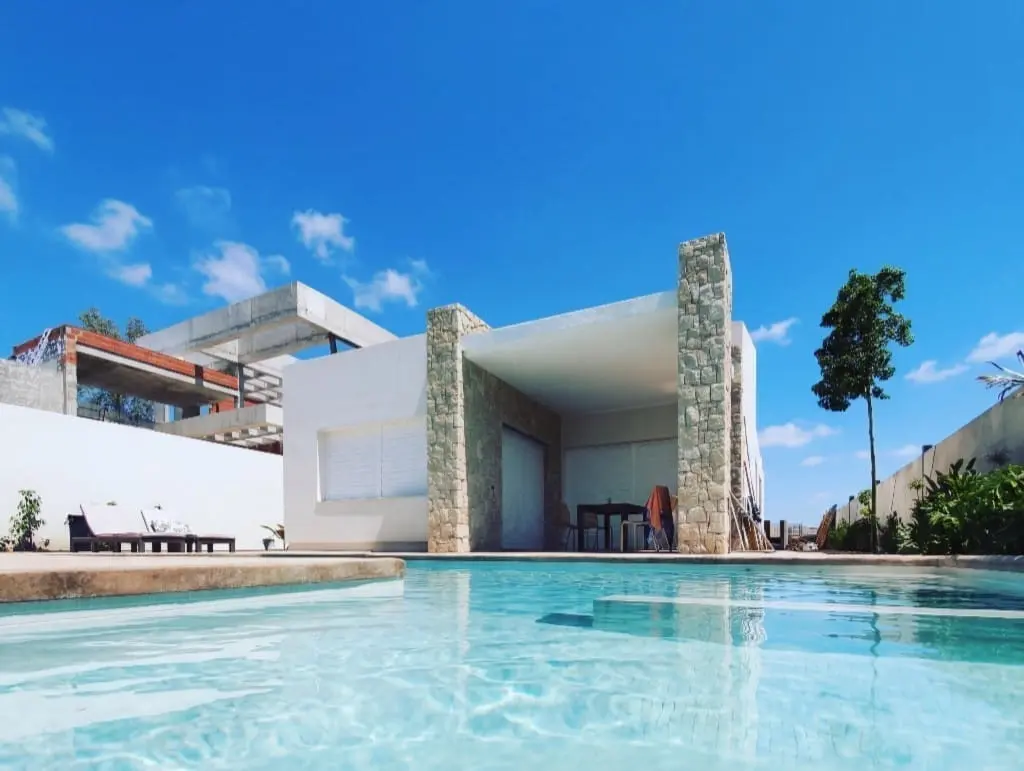 Piscina de agua transparente delante de una casa moderna con pilares de piedra y porche blanco