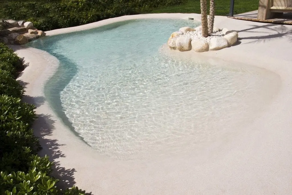 Entrada progresiva de una piscina de arena con agua cristalina y rocas decorativas