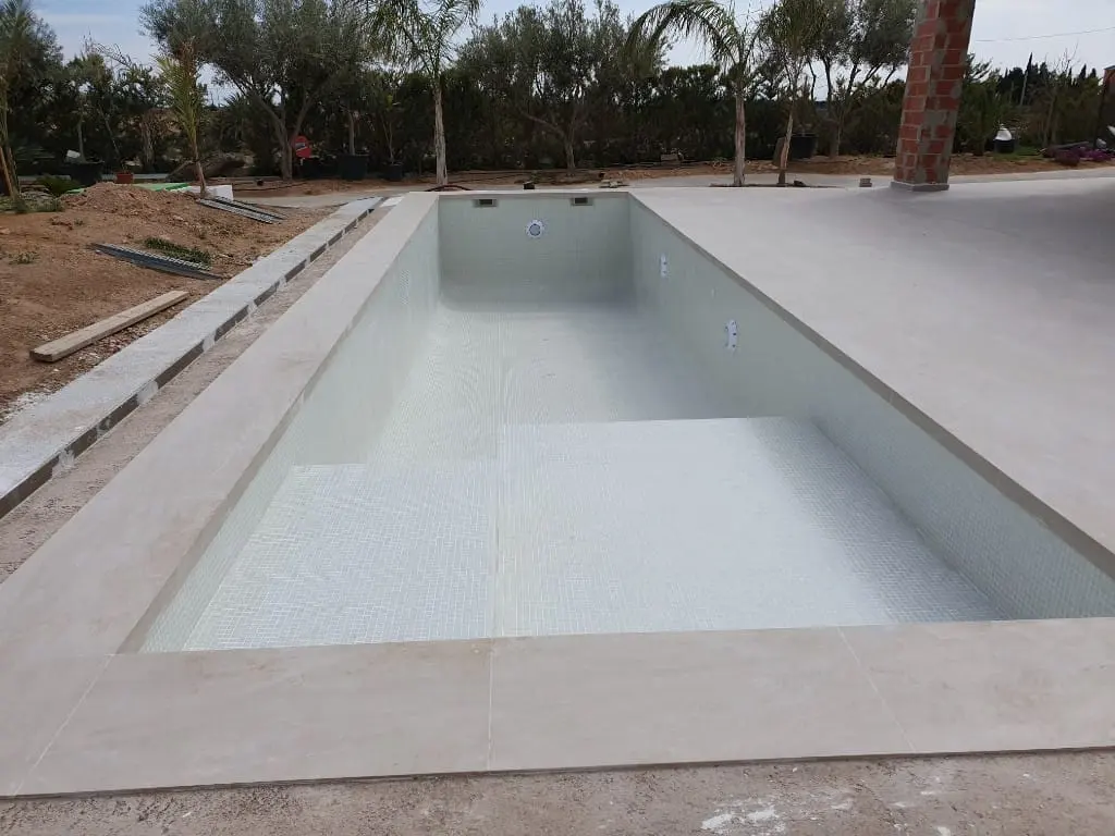Vaso de piscina vacío recién revestido con gresite blanco, con escalones y coronación de hormigón claro