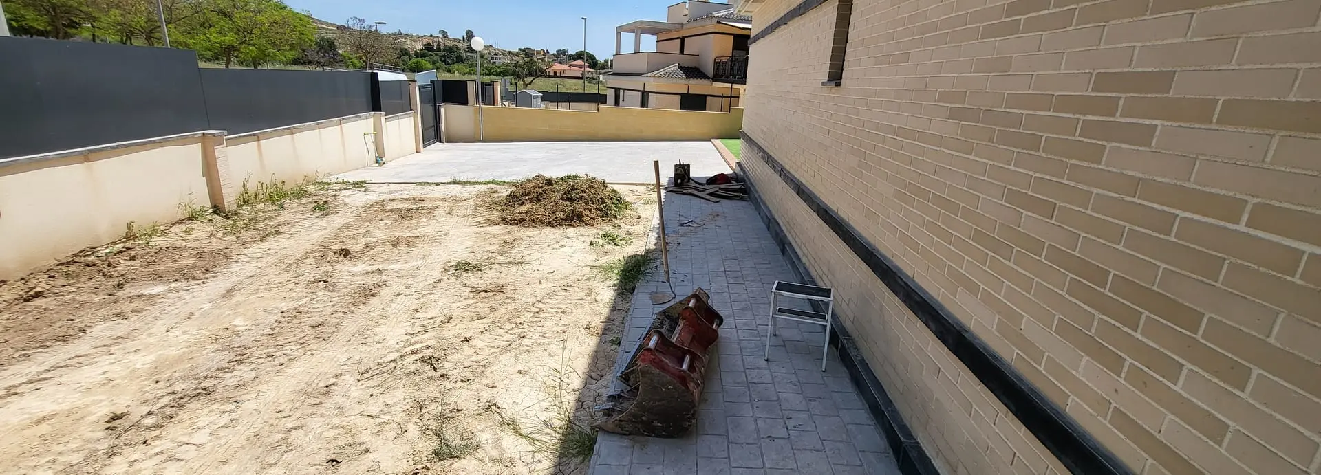 Antes: solar de tierra entre una pared de ladrillo y un muro, con restos de obra
