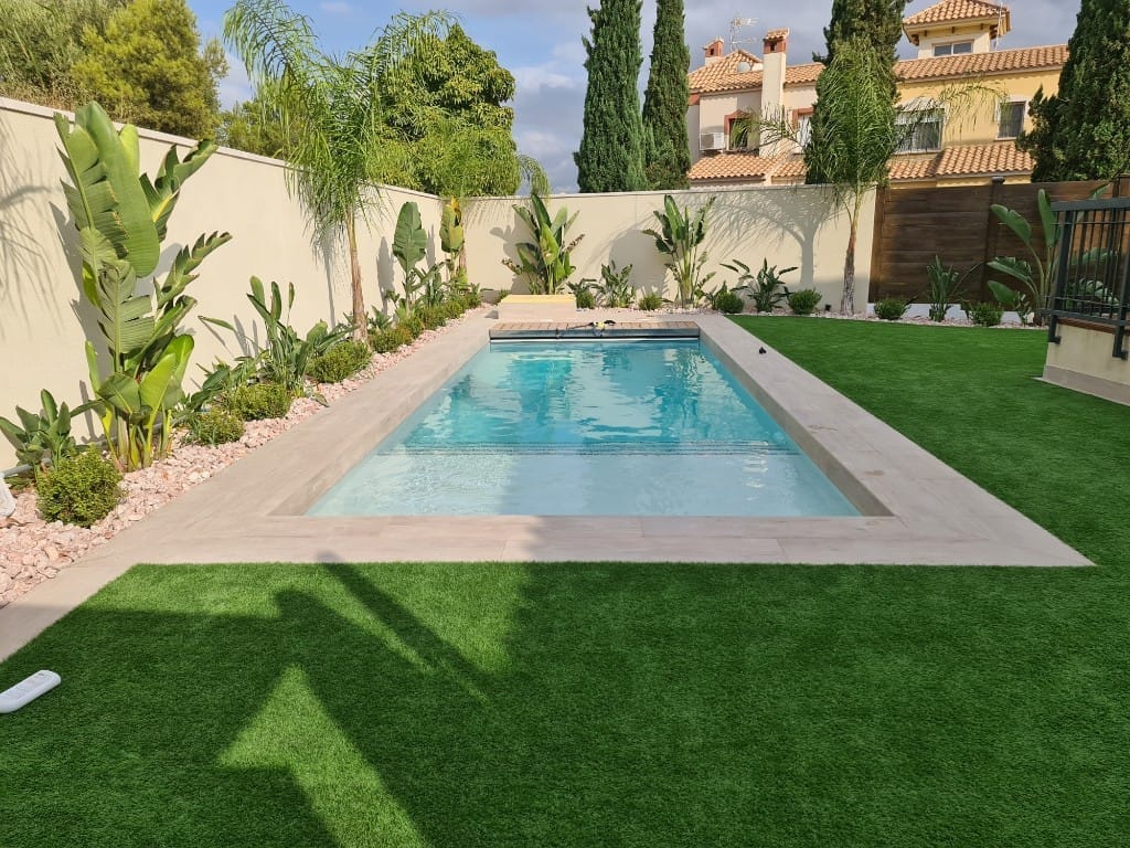 Piscina con césped artificial y vegetación tropical