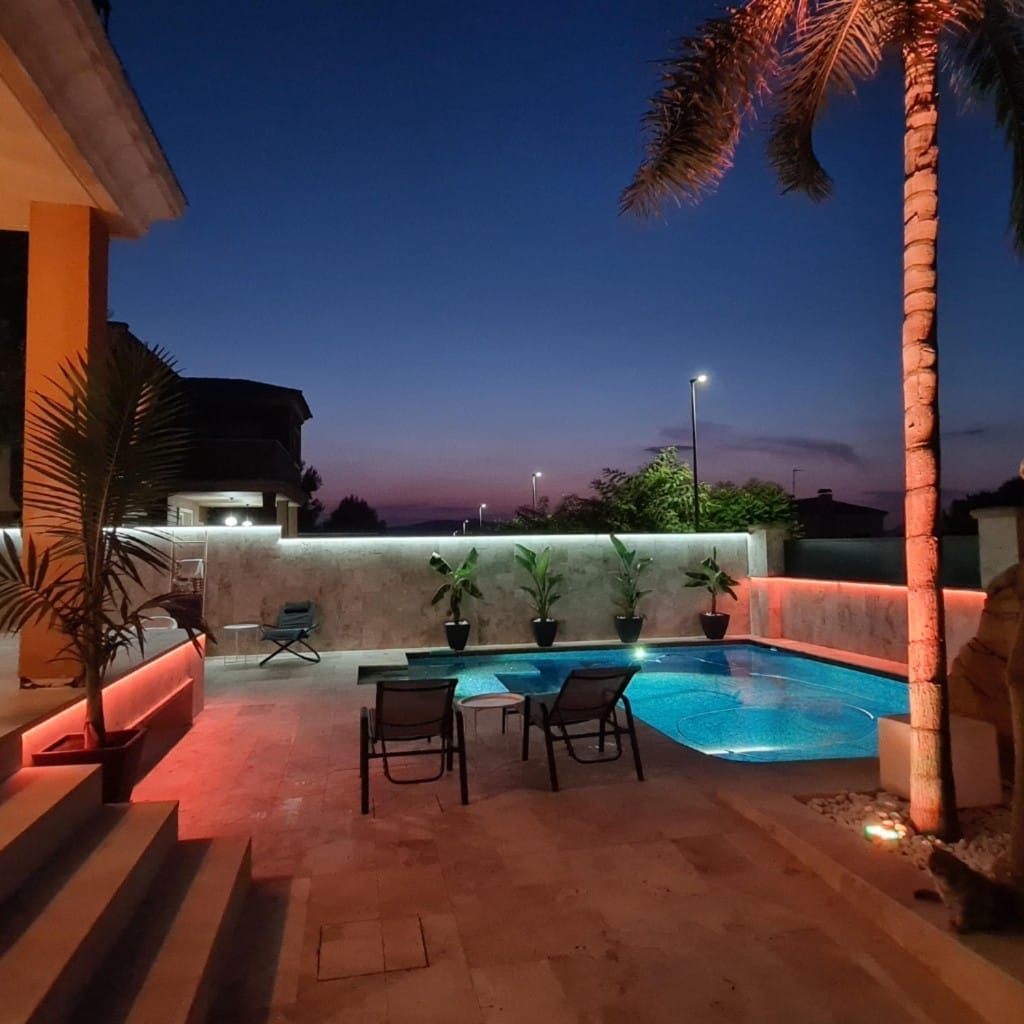 Piscina iluminada al atardecer con LED ámbar en muros y zona chill out en Alicante