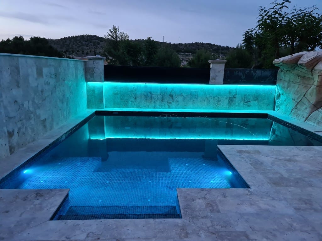 Piscina con LED turquesa al anochecer en Alicante