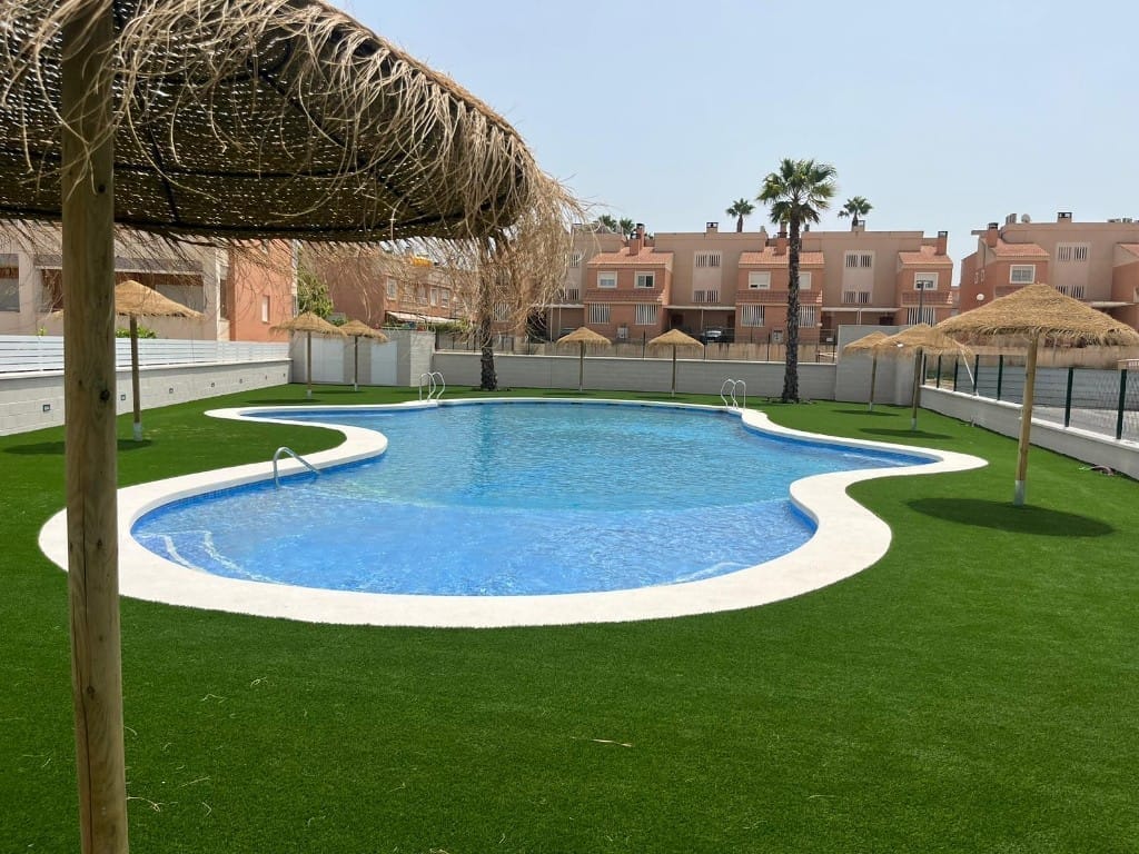 Piscina comunitaria terminada con revestimiento, césped artificial y zona de sombrillas